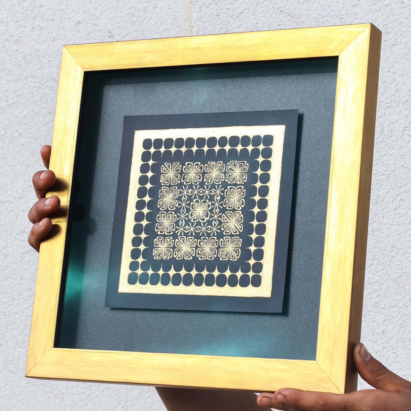Framed artwork with geometric pattern held by a person against a light gray background