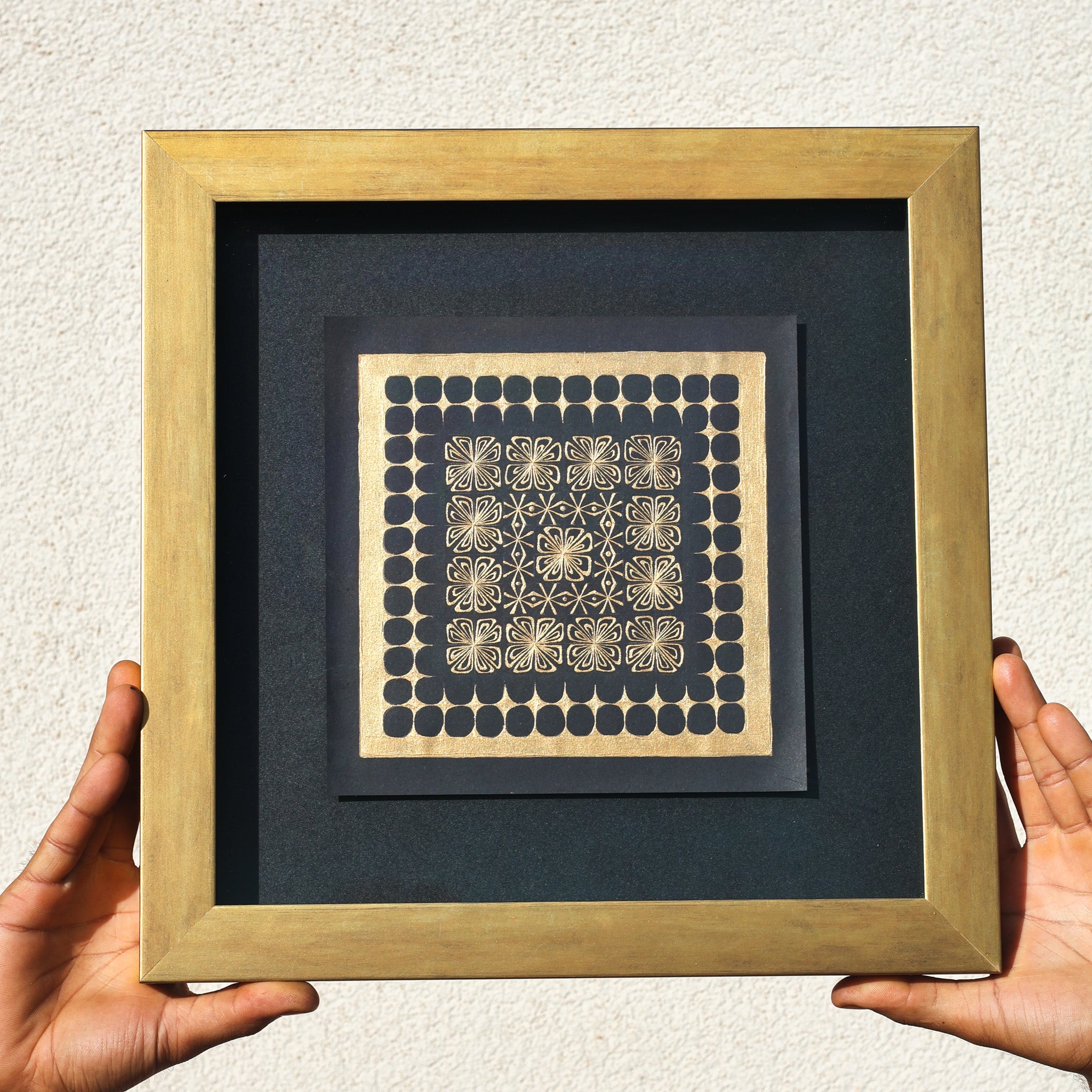 Framed artwork with geometric pattern held by hands against a neutral background