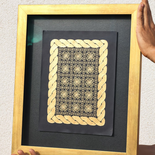 Framed artwork with gold geometric design on a black background, held by a person.