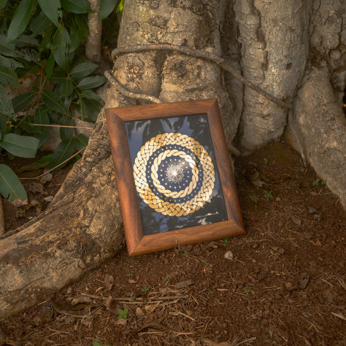 Framed woven art piece leaning against a tree trunk outdoors